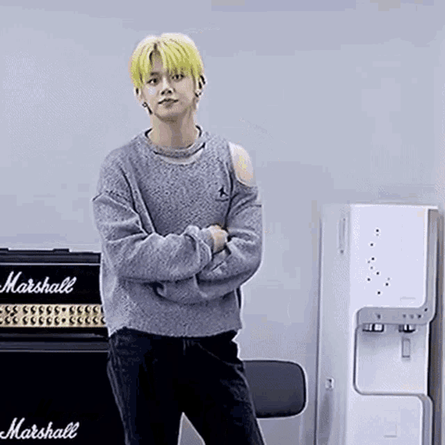 a man with yellow hair is standing in front of a marshall amplifier .