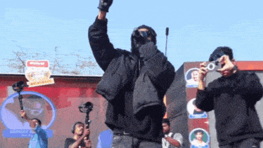 a man in a black jacket stands in front of a sign that says eminay
