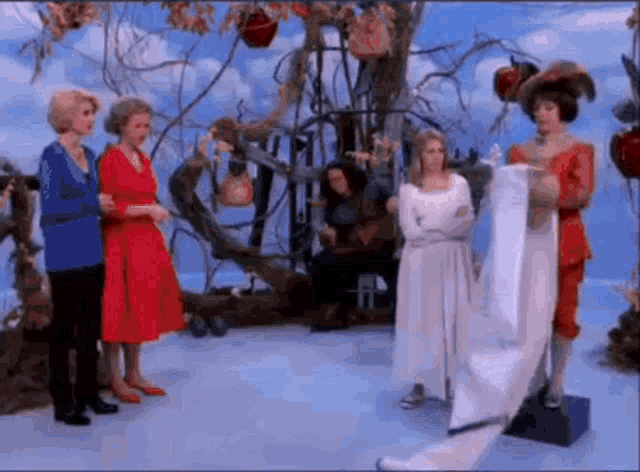 a woman in a white dress is standing in front of a group of women .