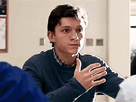 a young man in a blue sweater is sitting at a table with his hands folded .
