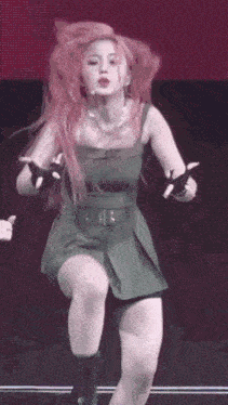 a woman with red hair is dancing on a stage wearing a green dress and black boots .