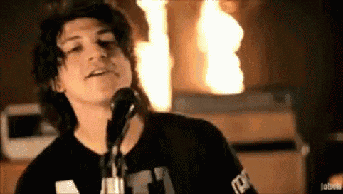 a young man is singing into a microphone while playing a guitar in front of a fire .