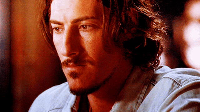 a man with long hair and a beard is looking at the camera