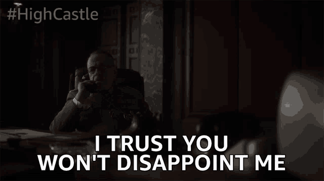 a man is sitting at a desk talking on a phone and says `` i trust you won 't disappoint me ''