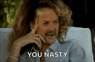 a man with long hair and a mustache is sitting in a chair with his hand on his head and says `` you nasty '' .
