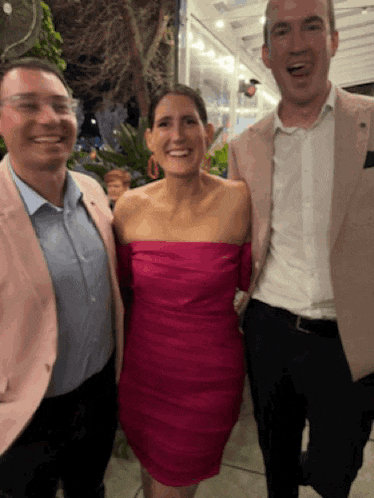 a woman in a pink dress stands between two men