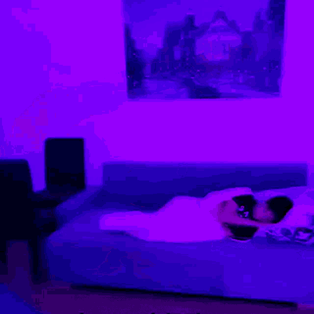 a blurry picture of a person laying on a bed with purple lights behind them .