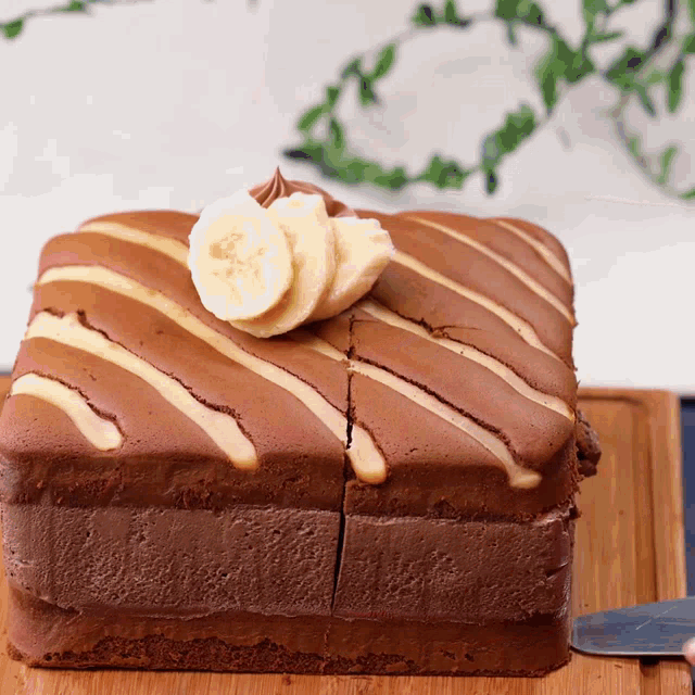 a chocolate cake with banana slices on top is sitting on a wooden cutting board