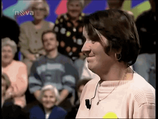 a woman wearing a pink sweater and earrings stands in front of a crowd of people with nova written on the screen behind her