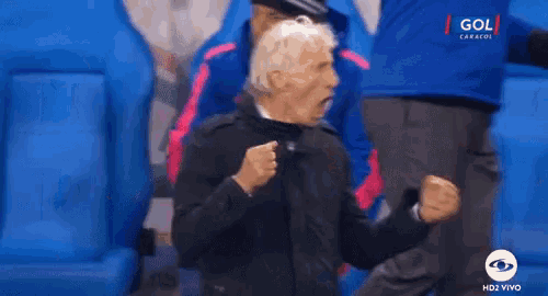 a man in a black jacket is celebrating a goal during a soccer match .