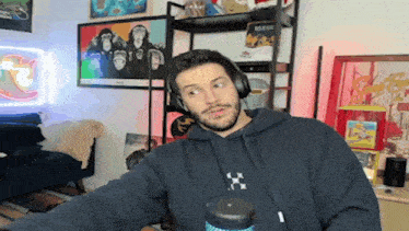 a man wearing headphones and a black hoodie is standing in front of a microphone .