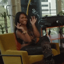 a woman is sitting in a yellow chair smiling and waving