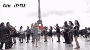 a group of people dancing in front of the eiffel tower in paris .