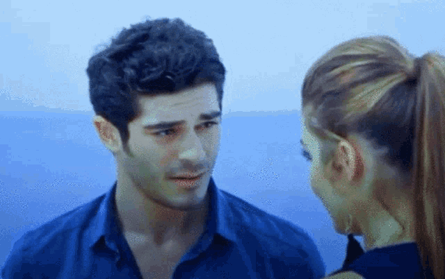 a man and a woman looking at each other with the ocean in the background