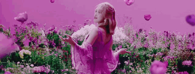 the woman is wearing a purple dress and standing in a field of flowers .