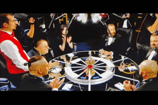 a group of men sitting around a table with a roulette wheel in the middle