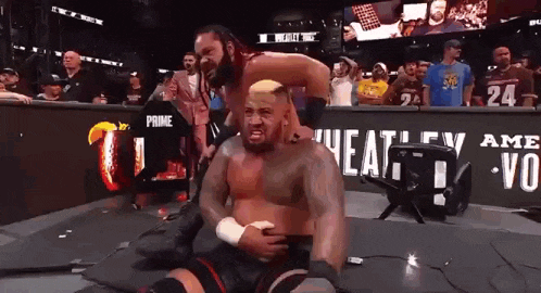 two men are wrestling in a wrestling ring and one of them is holding the other 's belly .