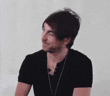 a man wearing a black shirt and a necklace looks to the side