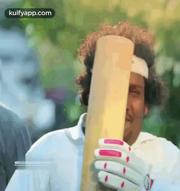 a man wearing a headband is holding a cricket bat in front of his face .