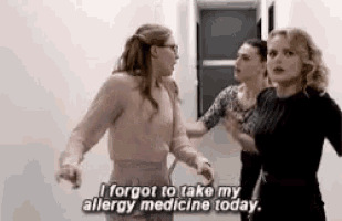three women are standing next to each other in a hallway . one of the women is talking about her allergy medicine .