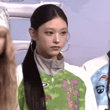 a woman wearing hoop earrings and a green jacket with the letter t on the front