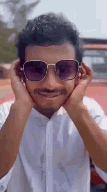 a man wearing sunglasses and a fake mustache is covering his ears .