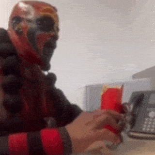 a person wearing a mask is sitting at a desk with a phone and a box of mcdonald 's fries .