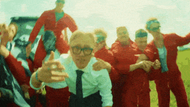 a man in a white shirt and tie is surrounded by a group of people in red jumpsuits