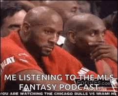 a group of men are sitting in a stadium and one of them is listening to the mls fantasy podcast .