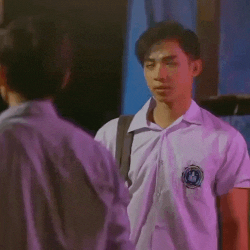 a man in a school uniform is standing next to another man in a purple shirt .