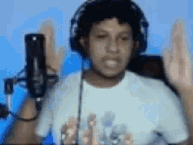 a man wearing headphones and a white shirt is standing in front of a microphone with his hands in the air .