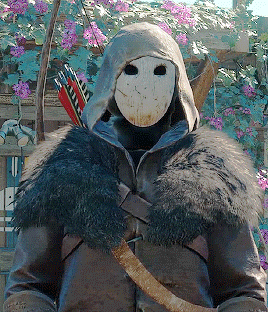 a man wearing a mask and a fur coat holds a bow and arrows