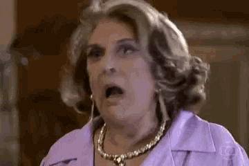 a woman wearing a purple shirt and a necklace is making a funny face .