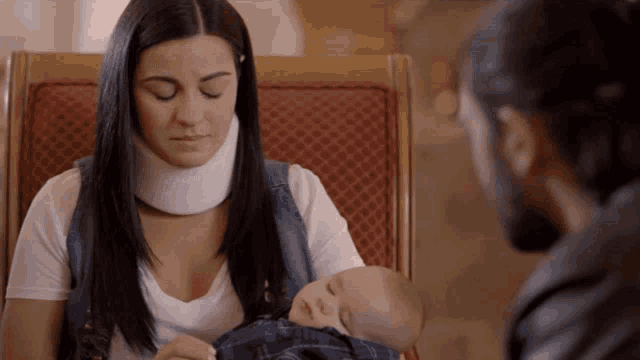 a woman wearing a neck brace holds a baby in her lap