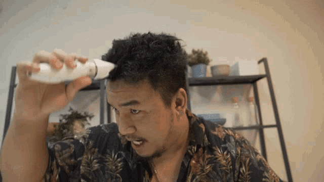 a man in a hawaiian shirt is using a hair clipper to cut his hair