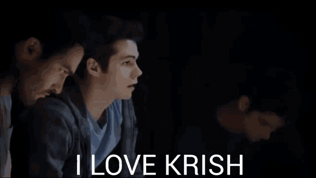 a man is sitting in a dark room with the words `` i love krish '' written on the bottom of the screen .