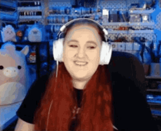 a woman with red hair is wearing headphones and smiling while sitting in front of a computer .