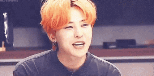 a young man with orange hair and earrings is smiling .