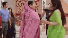 a woman in a pink dress is standing next to another woman in a green saree .