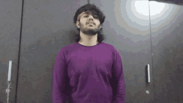 a man wearing a purple shirt and a headband is standing in front of a wall .