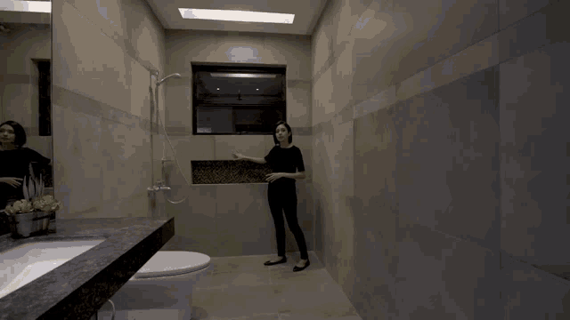 a woman stands in a bathroom next to a toilet and sink