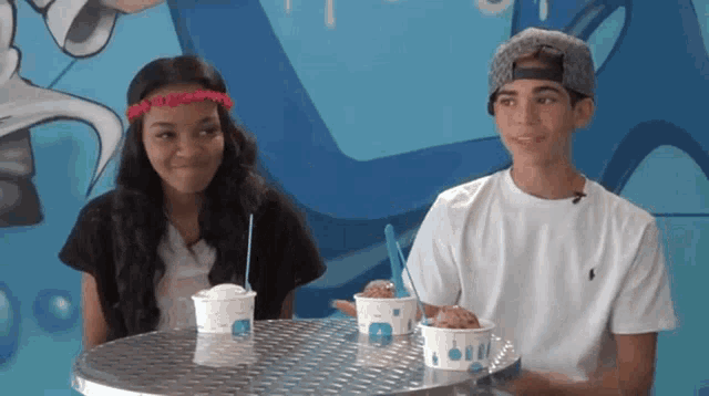 a boy and a girl are sitting at a table with ice cream cups