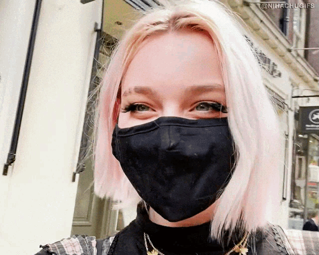 a woman wearing a black face mask is smiling in front of a sign that says no smoking