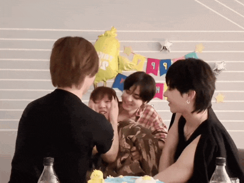 a group of people sitting around a table with balloons and a banner that says ' happy birthday ' on it