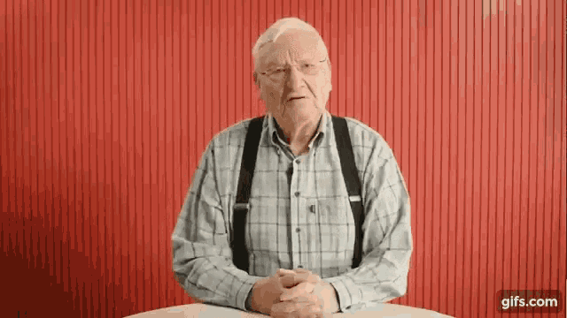 an older man wearing suspenders is sitting at a table