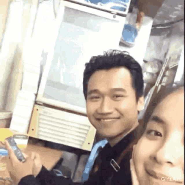 a man and a woman are posing for a picture while the man holds a cell phone .