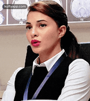 a woman in a white shirt and black vest is sitting in front of a wall with brain scans .