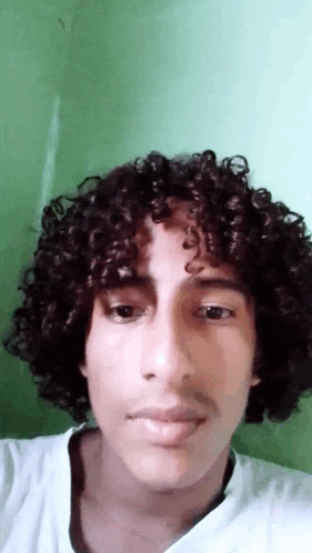 a young man with curly hair is taking a selfie with a green background .