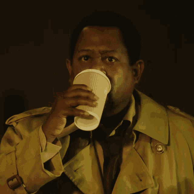 a man in a trench coat is drinking out of a paper cup