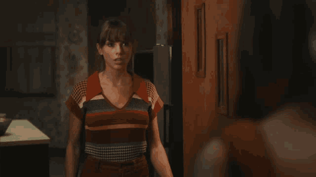 a woman in a striped shirt stands in a kitchen